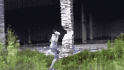 A Man Is Standing In Front Of A Large Stone Pillar In A Field . GIF