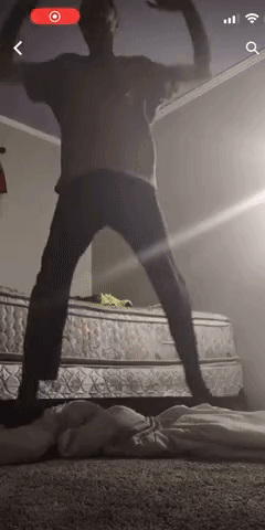 A Man Is Standing In Front Of A Mattress In A Room . GIF