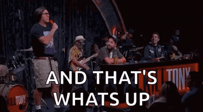 A Man Is Standing In Front Of A Microphone On A Stage With A Band Behind Him . GIF