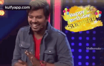 A Man Is Standing In Front Of A Microphone With Balloons And A Happy Birthday Message . GIF
