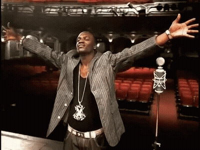 A Man Is Standing In Front Of A Microphone With His Arms Outstretched In An Auditorium GIF