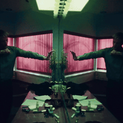 A Man Is Standing In Front Of A Mirror With A Pink Window Behind Him GIF