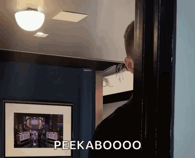 A Man Is Standing In Front Of A Picture That Says Peekaboooo On It GIF