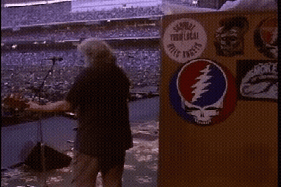 A Man Is Standing In Front Of A Podium With A Grateful Dead Sticker On It In A Stadium . GIF