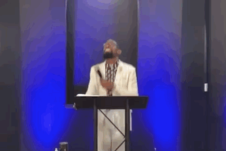 A Man Is Standing In Front Of A Podium With A Microphone And A Woman Is Standing Behind Him . GIF