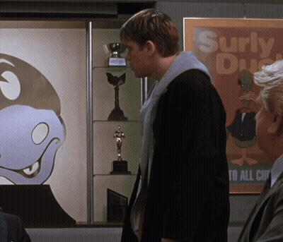 A Man Is Standing In Front Of A Poster That Says Surly Duck GIF