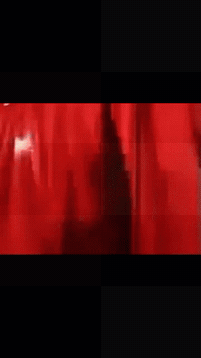 A Man Is Standing In Front Of A Red Curtain In A Dark Room . GIF