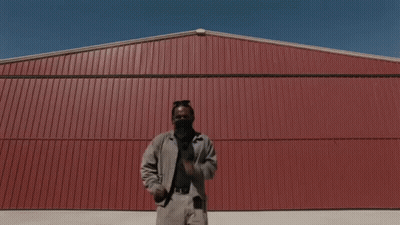 A Man Is Standing In Front Of A Red Wall GIF
