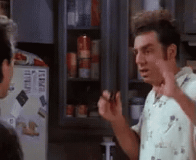 A Man Is Standing In Front Of A Refrigerator Talking To Another Man In A Kitchen . GIF