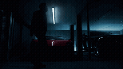 A Man Is Standing In Front Of A Row Of Cars In A Dark Garage GIF