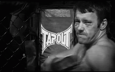 A Man Is Standing In Front Of A Sign That Says Tapout On It . GIF