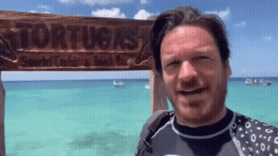 A Man Is Standing In Front Of A Sign That Says Tortuga 'S GIF