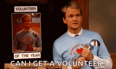 A Man Is Standing In Front Of A Sign That Says Volunteer Of The Year And Holding A Magnifying Glass . GIF