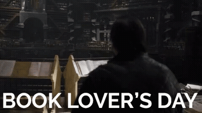 A Man Is Standing In Front Of A Stack Of Books In A Library . GIF