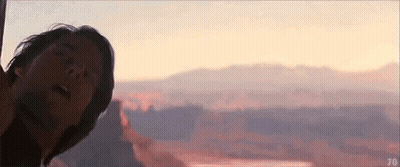 A Man Is Standing In Front Of A Sunset Over A Canyon . GIF