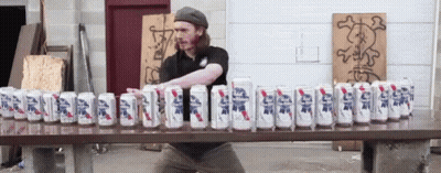 A Man Is Standing In Front Of A Table Full Of Cans Of Beer GIF