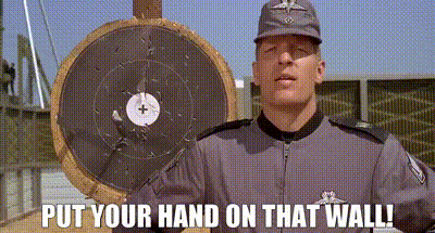 A Man Is Standing In Front Of A Target With The Words `` Put Your Hand On That Wall '' . GIF