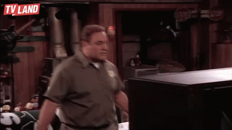 A Man Is Standing In Front Of A Television In A Room With A Tv Land Sign Above Him . GIF