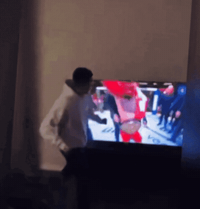 A Man Is Standing In Front Of A Television With A Blurry Picture Of People On It GIF