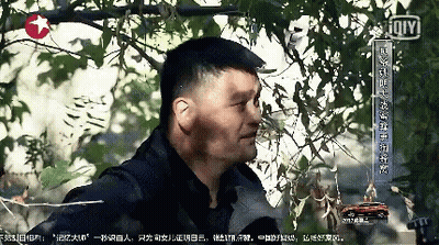 A Man Is Standing In Front Of A Tree With Chinese Writing On The Bottom Right GIF