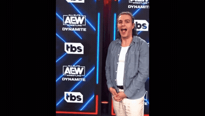 A Man Is Standing In Front Of A Wall That Says Aew GIF