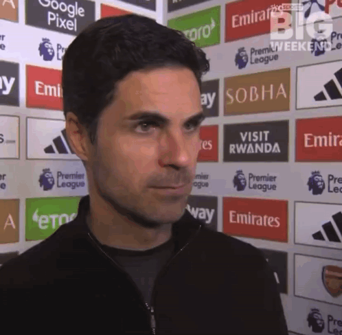 A Man Is Standing In Front Of A Wall With Emirates Advertisements On It GIF