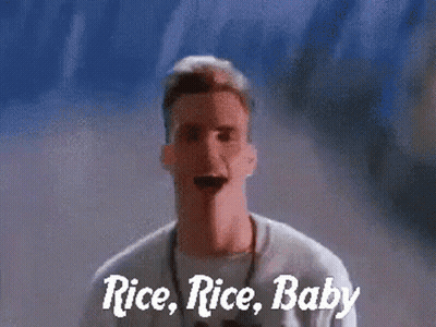 A Man Is Standing In Front Of A Wall With The Words Rice Rice Baby Written On It GIF