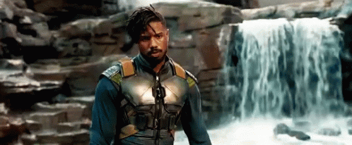 A Man Is Standing In Front Of A Waterfall . GIF