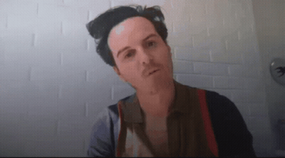 A Man Is Standing In Front Of A White Brick Wall Looking At The Camera . GIF