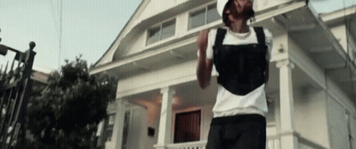 A Man Is Standing In Front Of A White House Wearing A Backpack . GIF