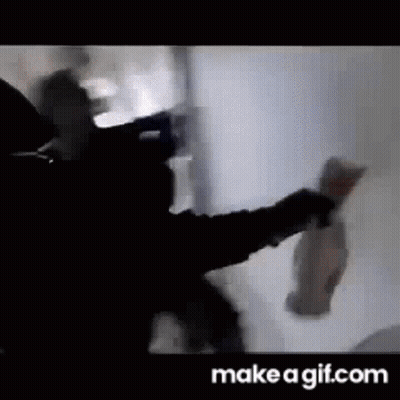 A Man Is Standing In Front Of A White Wall Holding A Bottle Of Beer . GIF