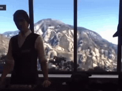 A Man Is Standing In Front Of A Window With A Mountain In The Background GIF