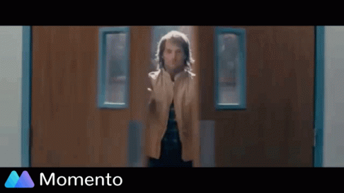 A Man Is Standing In Front Of A Wooden Door In A Hallway . GIF