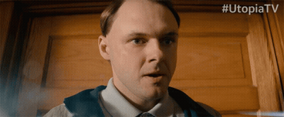 A Man Is Standing In Front Of A Wooden Door With # Utopiatv Written Above Him GIF