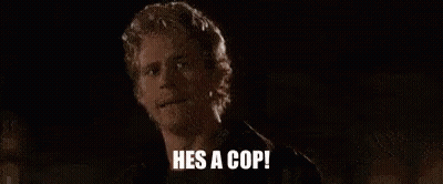 A Man Is Standing In The Dark With The Words `` He 'S A Cop '' Written On His Face . GIF