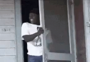 A Man Is Standing In The Doorway Of A Building Holding A Bottle Of Beer . GIF