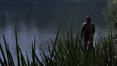 A Man Is Standing In The Grass Near A Lake GIF