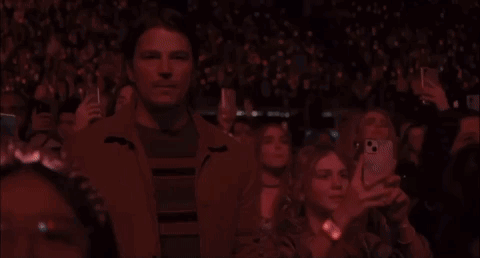 A Man Is Standing In The Middle Of A Crowd Of People Taking Pictures Of A Concert . GIF