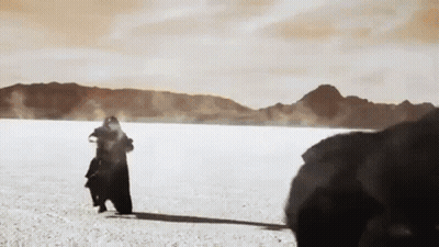 A Man Is Standing In The Middle Of A Desert Holding A Baby . GIF