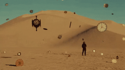 A Man Is Standing In The Middle Of A Desert With Clocks Flying Around Him . GIF