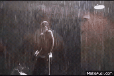 A Man Is Standing In The Rain With A Boxing Glove In His Hand . GIF