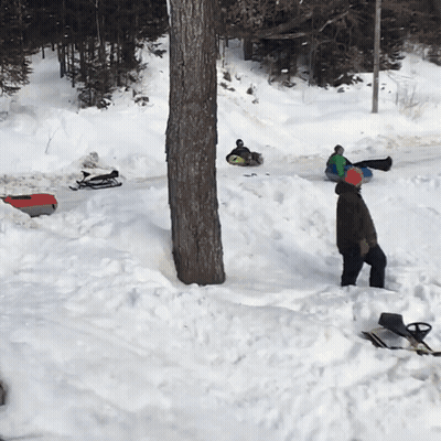A Man Is Standing In The Snow Near A Tree GIF