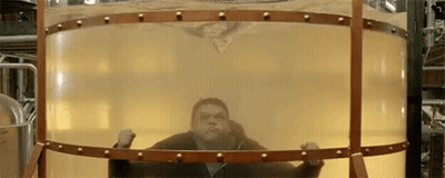 A Man Is Standing Inside Of A Large Cylindrical Container Filled With Liquid . GIF