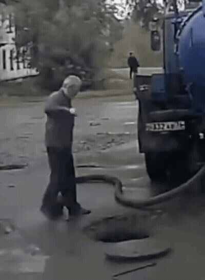 A Man Is Standing Next To A Blue Truck That Is Pumping Water Into A Manhole . GIF