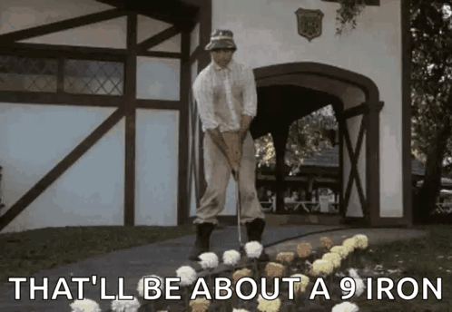 A Man Is Standing Next To A Bunch Of Flowers With The Words That 'Ll Be About A 9 Iron Below Him GIF