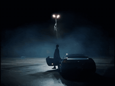 A Man Is Standing Next To A Car In A Dark Parking Lot GIF