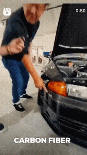 A Man Is Standing Next To A Car With The Hood Open And The Words Carbon Fiber Written Below Him GIF