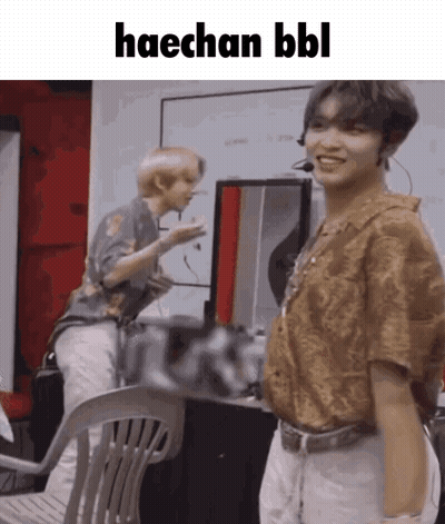A Man Is Standing Next To A Chair With The Words Haechan Bbl Written On It . GIF