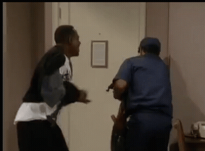 A Man Is Standing Next To A Police Officer In A Hallway Holding A Gun . GIF