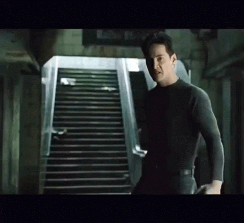 A Man Is Standing Next To A Set Of Stairs In A Dark Room . GIF